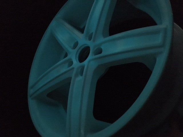 Powder-coated car wheel rim in the dark, glowing blue-green, application example