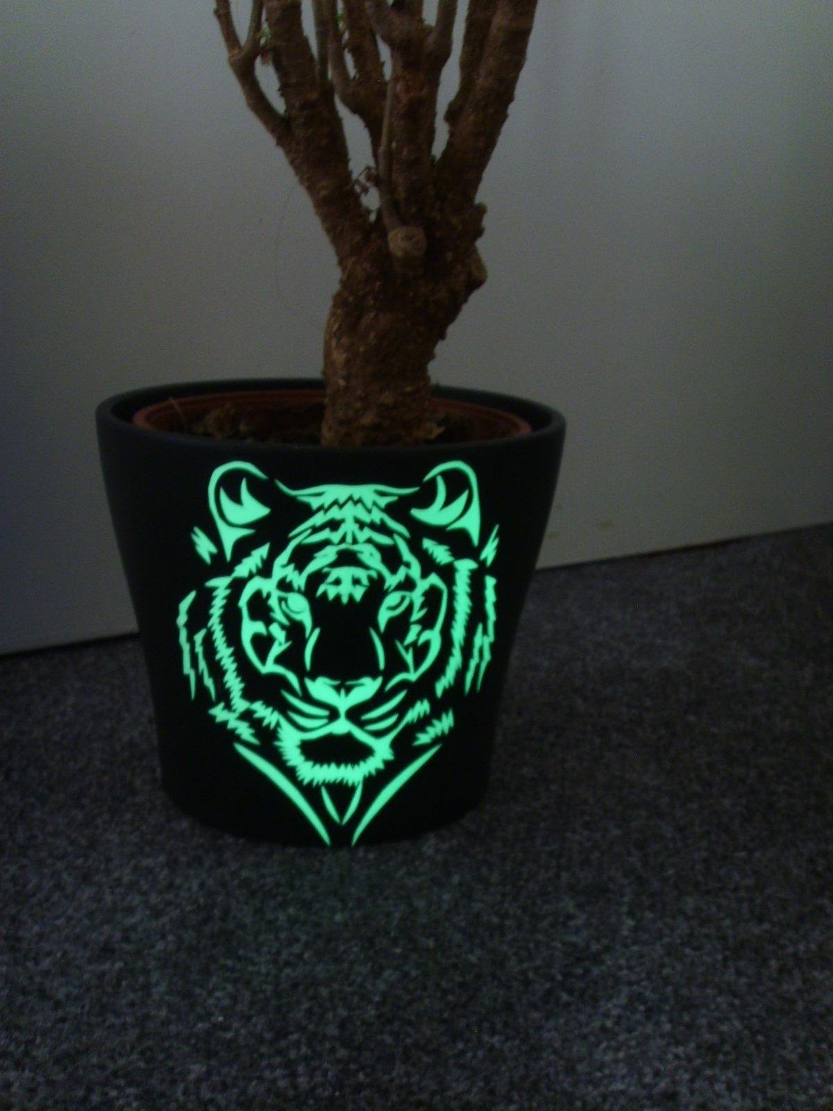 Black plant pot with a tiger head motif made from glow film, glowing green in the dark