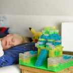 Building brick model on a green baseplate in daylight, a sleeping child in the background