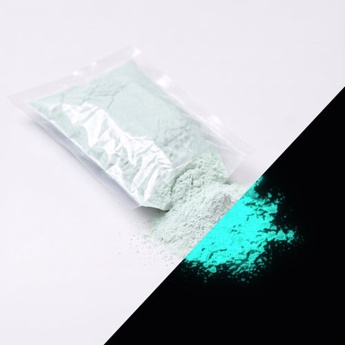 Fine glow pigment Natural Green-Blue 100 g: cut-open bag and a small heap of fine powder, whitish by day, glowing green-blue in the dark (lower right)