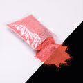 Fine glow pigment Red-Red 100 g: cut-open bag and a small heap of fine powder, light red by day, glowing reddish in the dark (lower right)