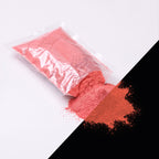 Fine glow pigment Red-Red 100 g: cut-open bag and a small heap of fine powder, light red by day, glowing reddish in the dark (lower right)