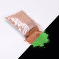 Fine glow pigment Terracotta 100 g: cut-open bag and a small heap of fine powder, brownish by day, glowing green in the dark (lower right)