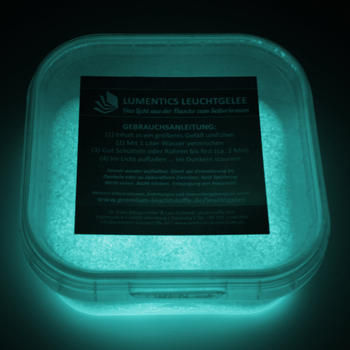 Glow Jelly Natural/Blue-Green in its tub in the dark, glowing blue-green, label showing as a dark panel