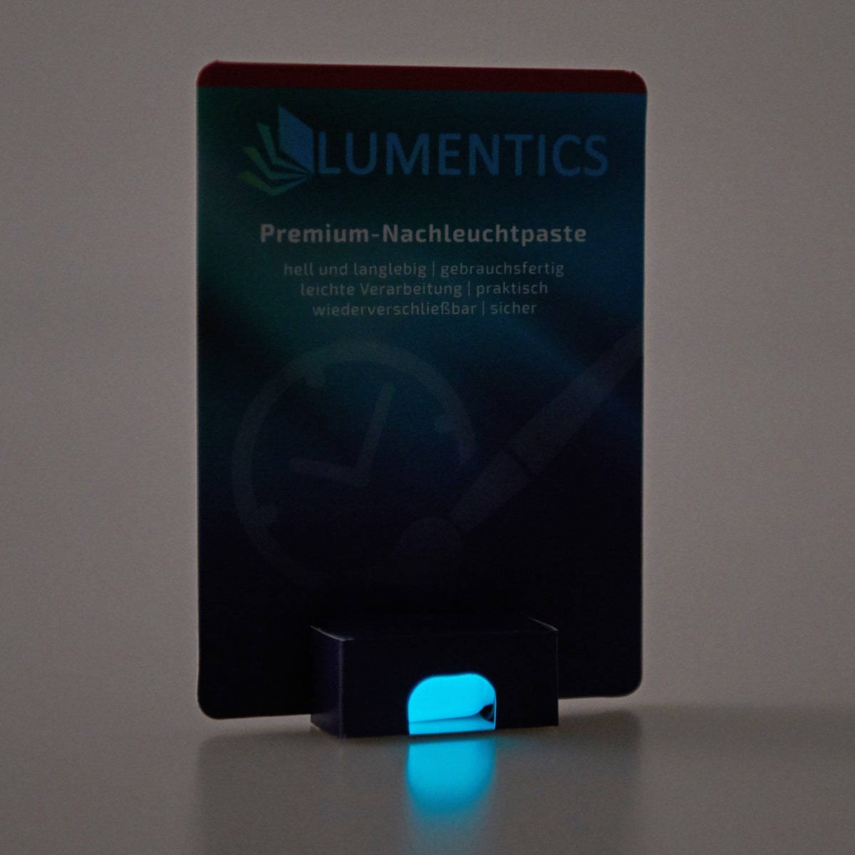 Luminous Paint for Watch Hands Natural Blue-Green 2 g: card in dim light, the paste in the holder glowing blue-green