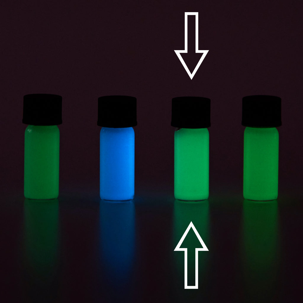 Four small vials with colour samples in the dark, glowing green and blue, arrows marking one vial