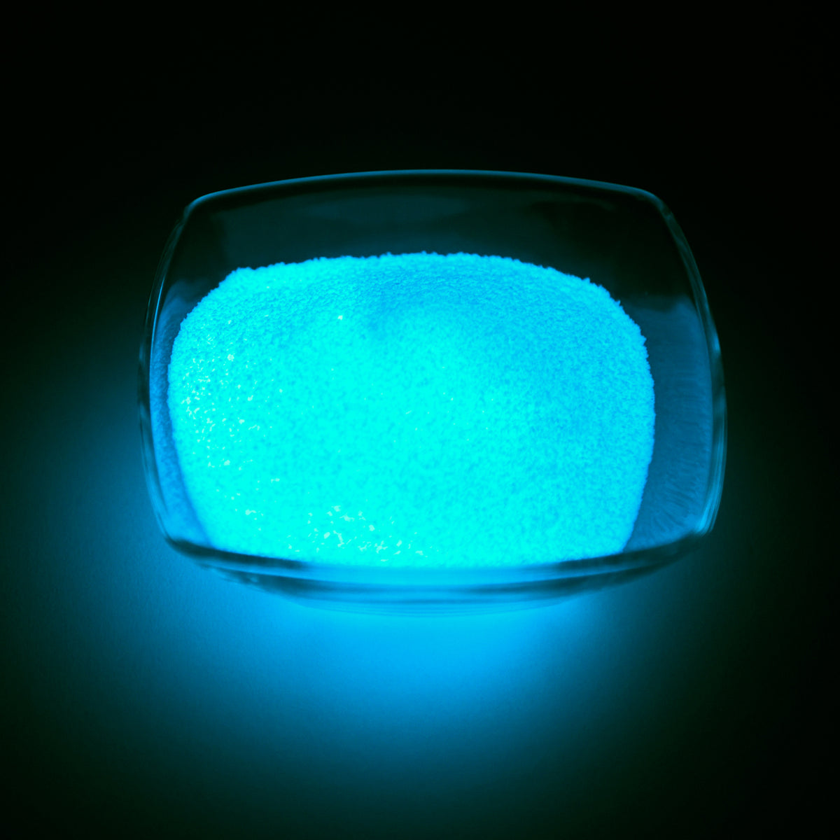 Glow Granules Blue 1 mm in a glass dish in the dark, glowing blue