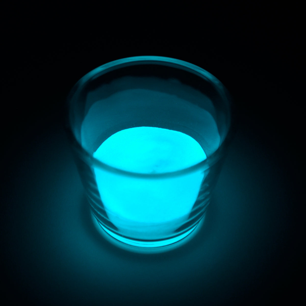 Glow Granules Blue 1 mm in a glass in the dark, glowing blue-green