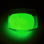 Glow Granules Green 1 mm, 100 g in a glass dish, glowing green in the dark