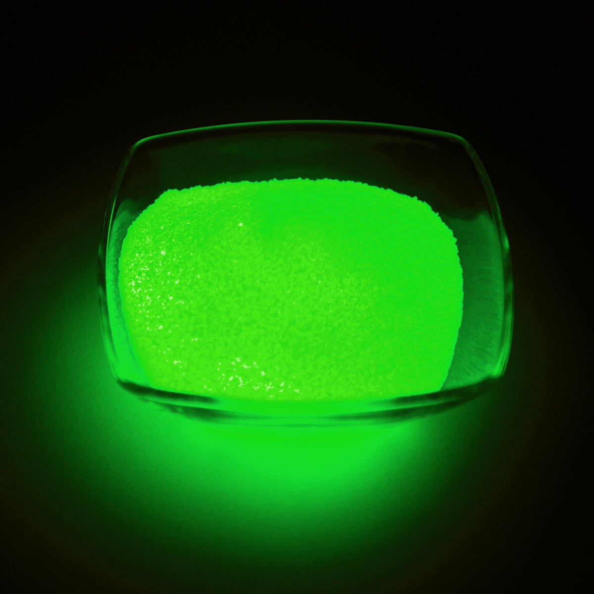 Glow Granules Green 1 mm, 100 g in a glass dish, glowing green in the dark
