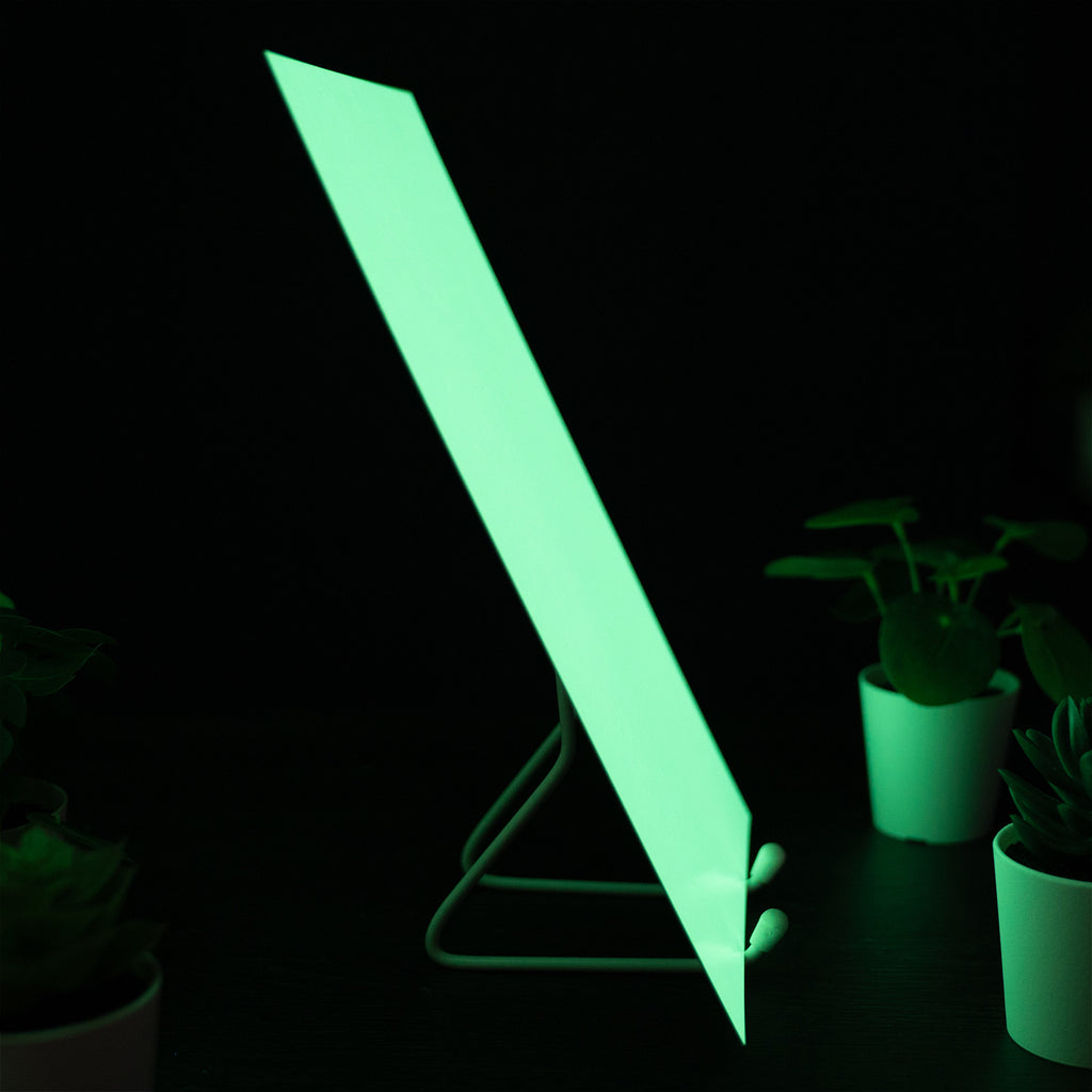 Glow Board A5 seen from the side on a wire stand in the dark, glowing green