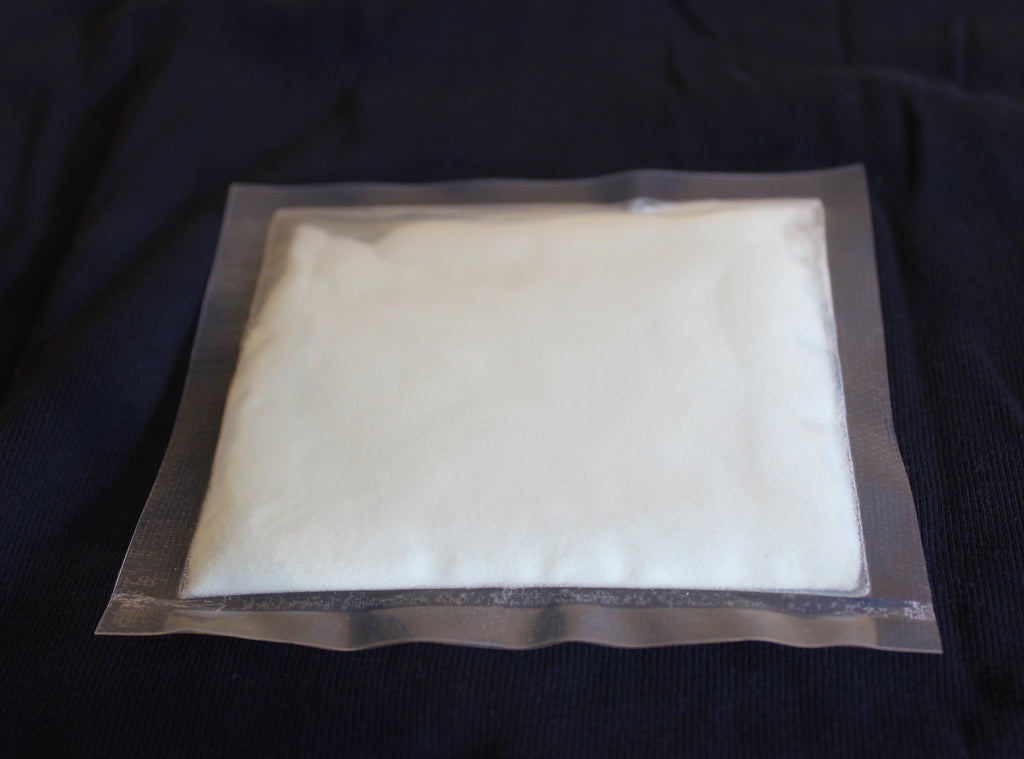Glow in the Dark Powder Blue-Green 40 g: pouch of white powder in daylight on dark fabric
