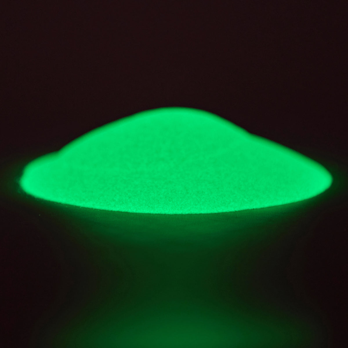 Glow in the Dark Powder Green-Green 40 g: small pile of powder in the dark, glowing green on a dark background