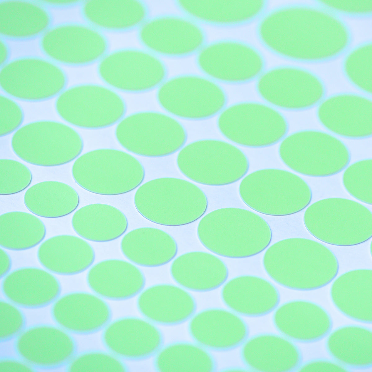 Glow dots in different sizes in close-up, glowing light green on a white sheet