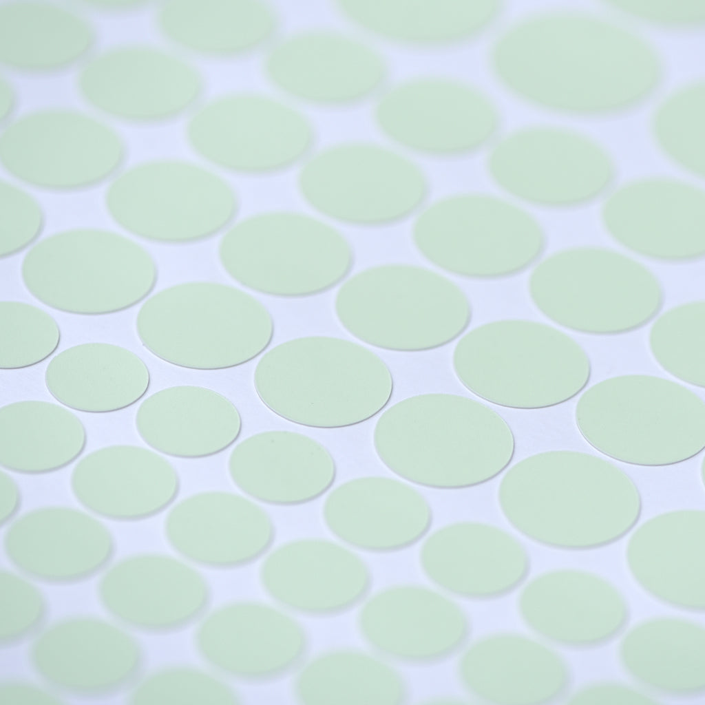 Glow dots in different sizes in close-up in daylight, pale green on a white sheet