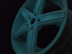 Powder-coated car wheel rim in the dark, glowing blue-green, application example