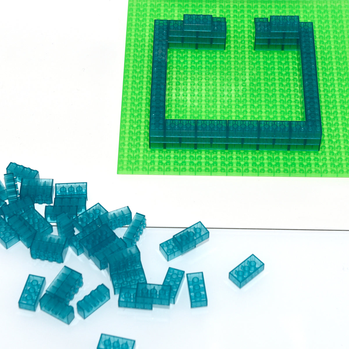 Blue 2x4 building bricks as a frame on a green baseplate, loose bricks in front on the table