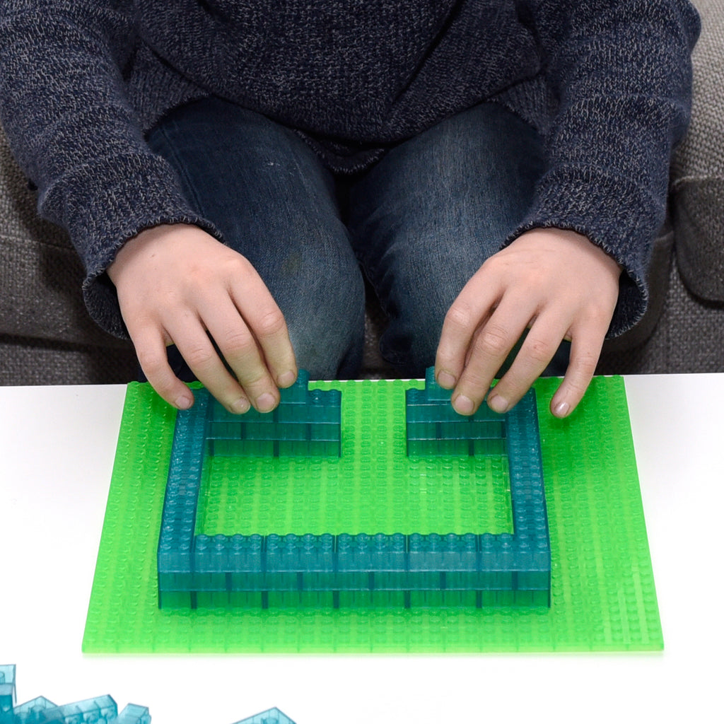 Child building a frame from blue 2x4 building bricks on a green baseplate