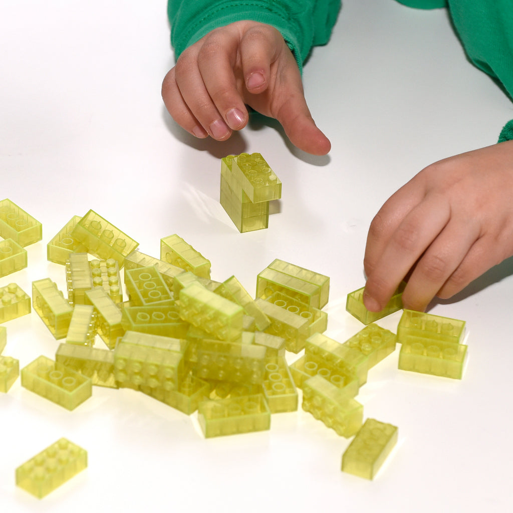 Two hands building with yellow 2x4 Building Bricks, more bricks loose on the table