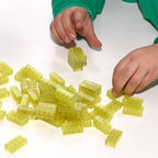 Two hands building with yellow 2x4 Building Bricks, more bricks loose on the table