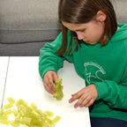 Child in a green jumper building a tower from yellow 2x4 Building Bricks at a white table