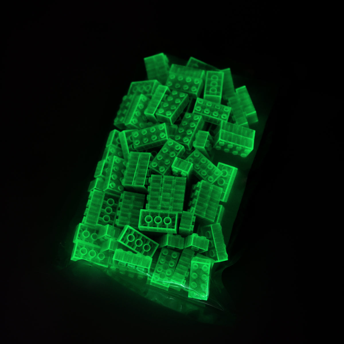 Bag of green 2x4 building bricks in the dark, the bricks glowing green through the film