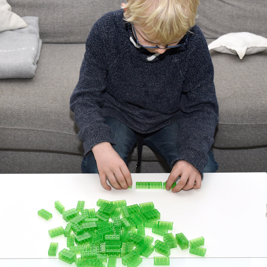 Child wearing glasses building at a white table with transparent green 2x4 building bricks