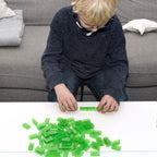 Child wearing glasses building at a white table with transparent green 2x4 building bricks