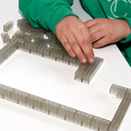 Transparent 2x4 building bricks in daylight, child's hand building a wall