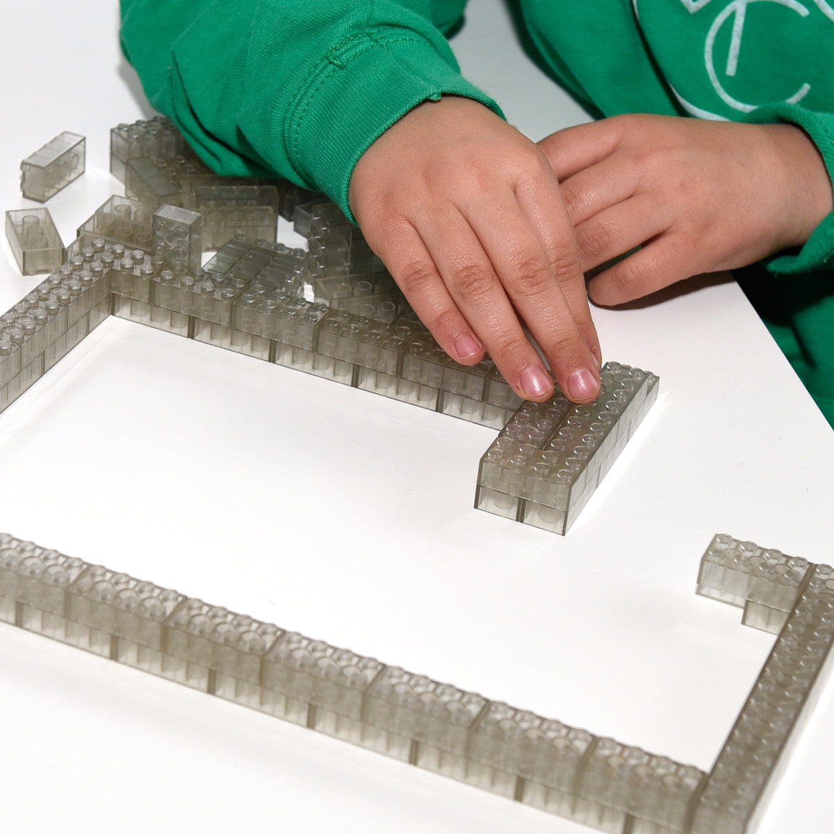Transparent 2x4 building bricks in daylight, child's hand building a wall