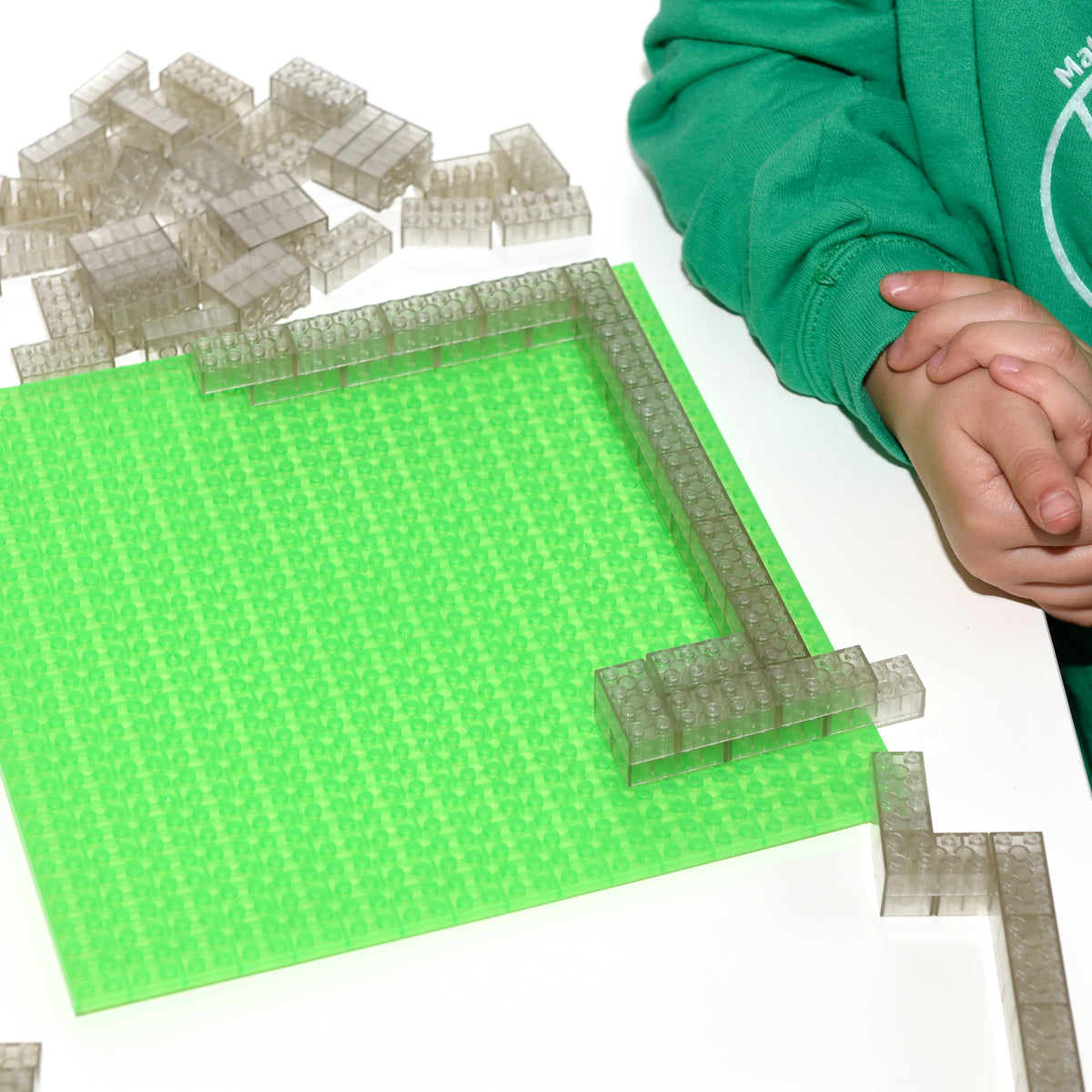 Child's hand assembling transparent 2x4 building bricks into a frame