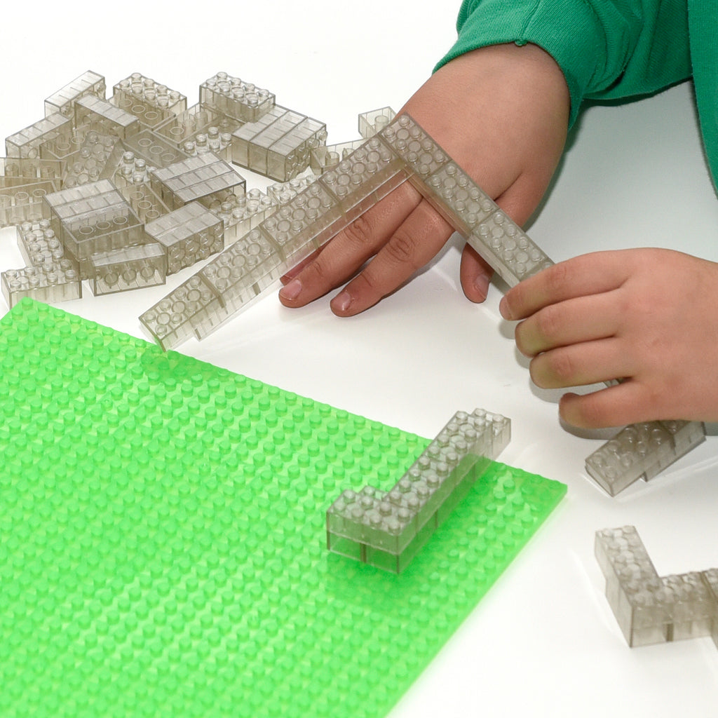 Transparent 2x4 building bricks on a green baseplate, children's hands building
