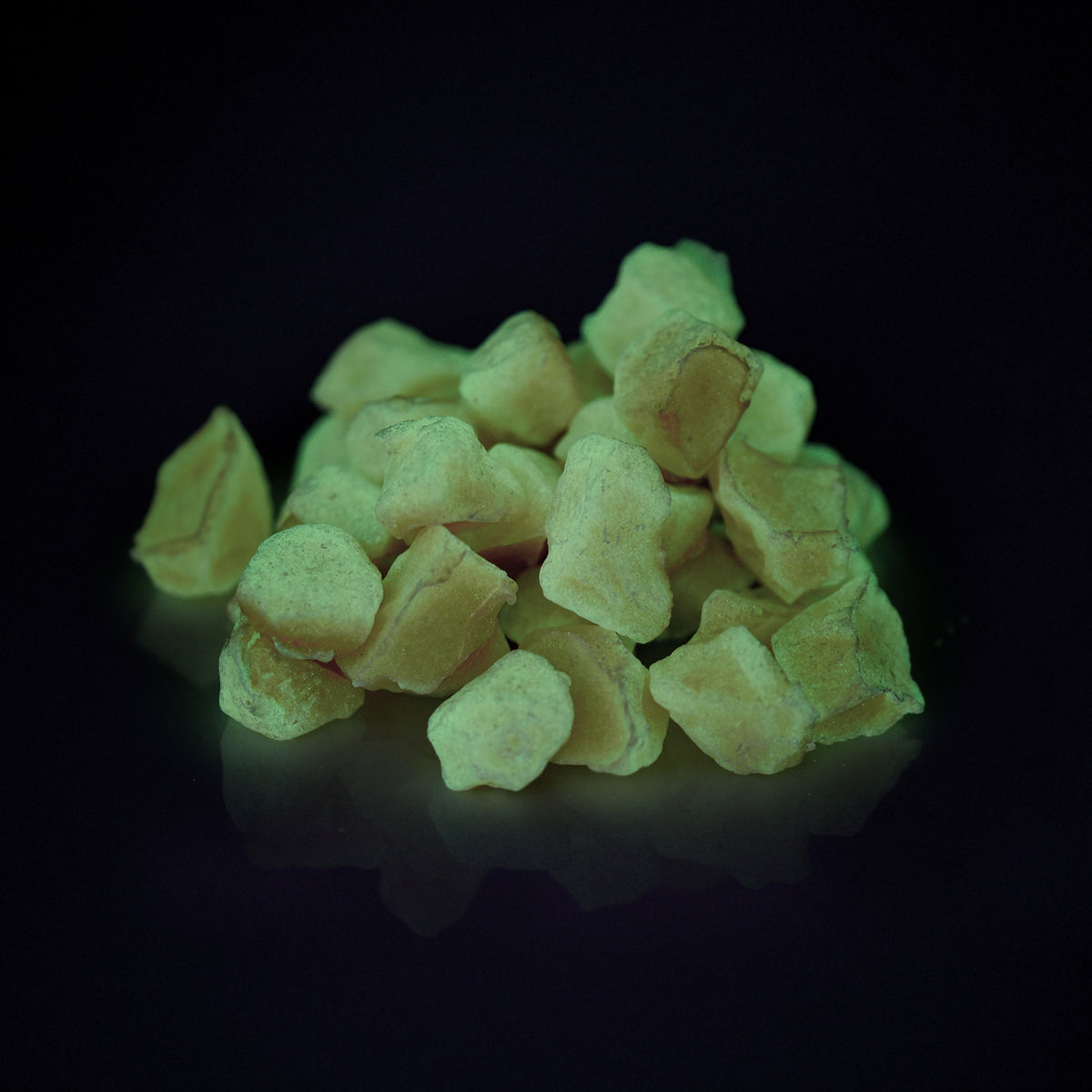Glow Stones Brown 300 g as a heap in the dark, glowing yellowish green